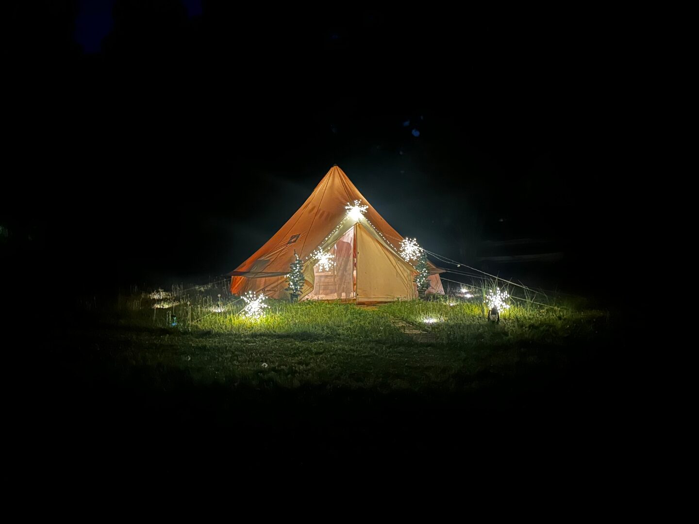 Bell tent exterior at night with sparkler lights illuminating the entrance.