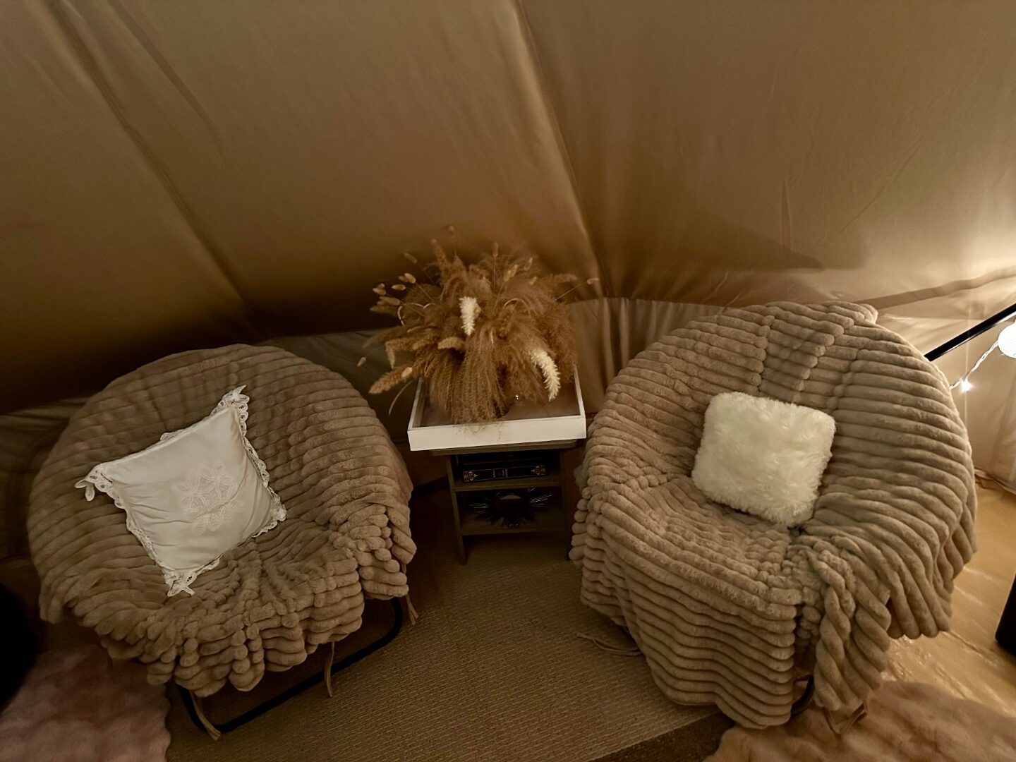 Two round plush chairs inside a bell tent with pampas grass centerpiece and soft textures.