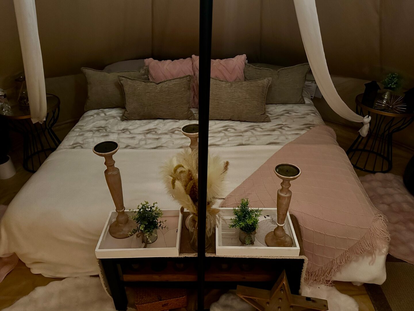 Bell tent bed styled for two with pink and sage pillows, wooden candlesticks and soft lantern light.